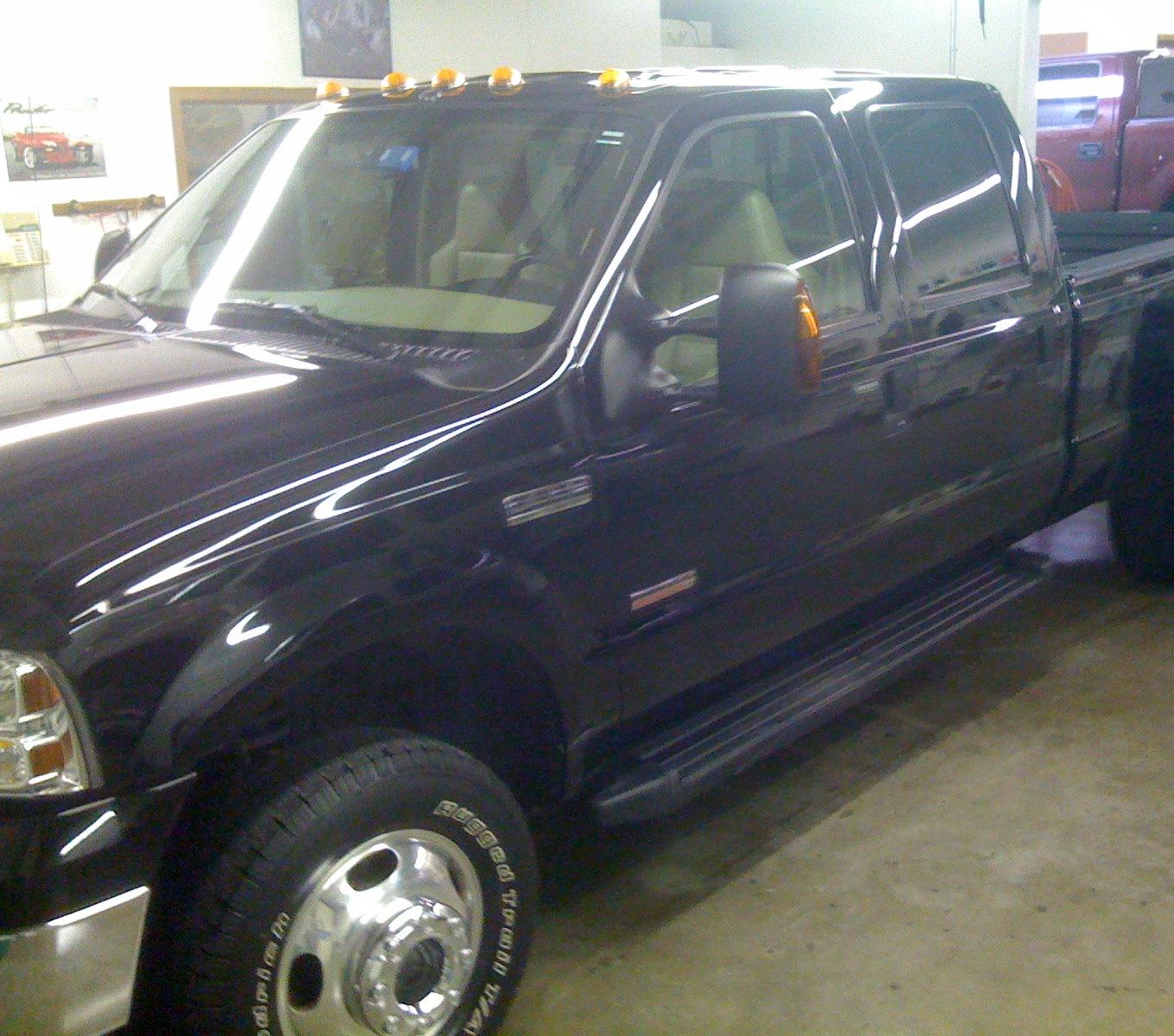 A black crew-cab dually finished inside the shop, the paint reflecting the ceiling lights