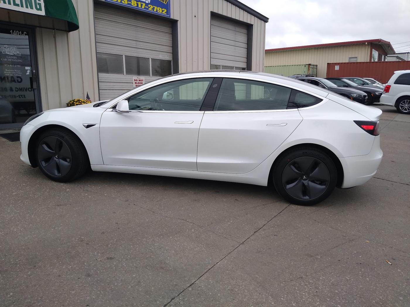 A white Tesla Model 3 finished and parked outside the Gaines Car Detailing door